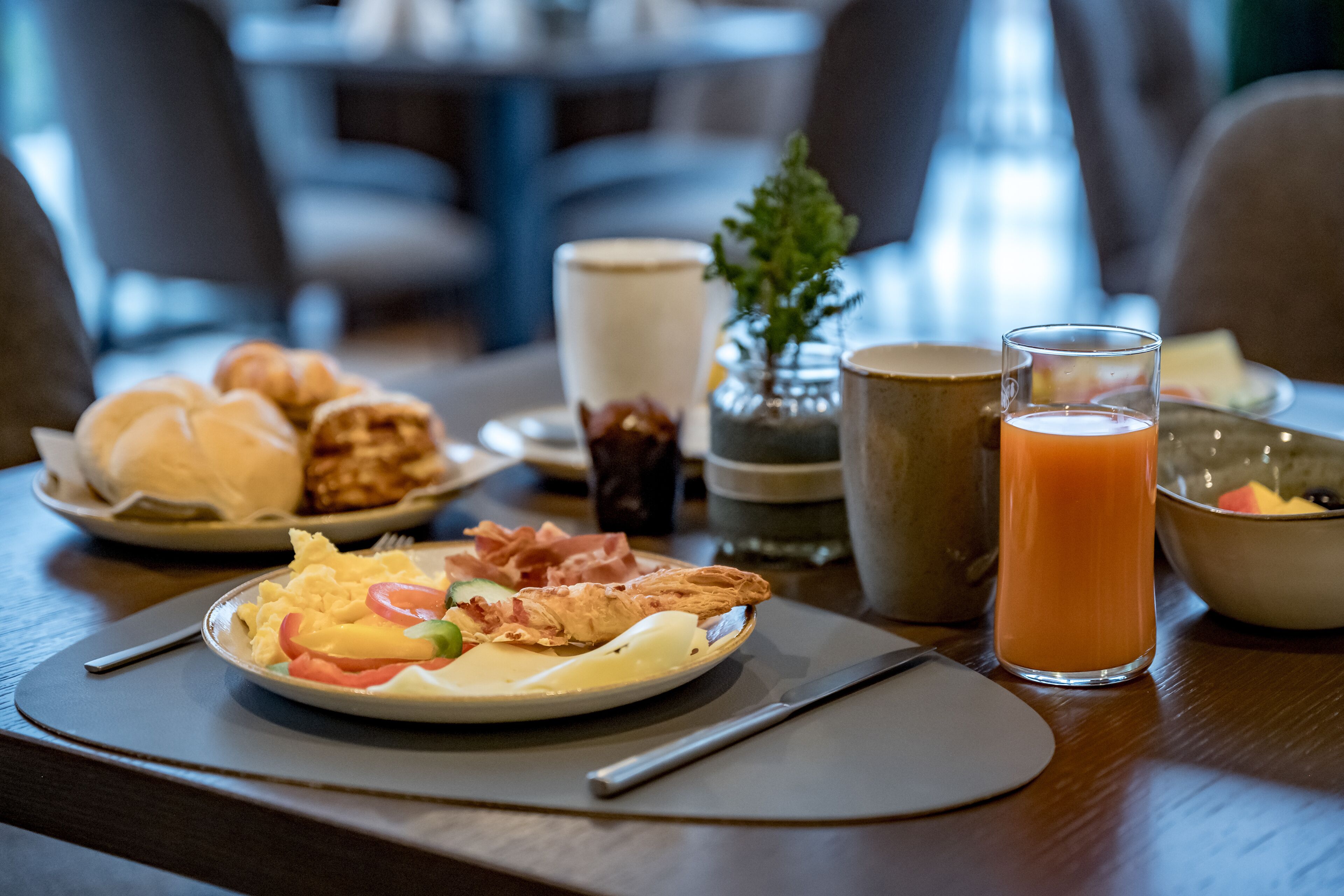 A breakfast setting with croissants, eggs, bacon, and a glass of orange juice on a wooden table.