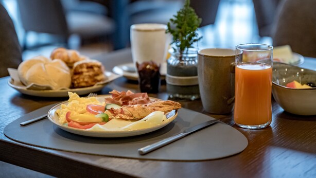 A breakfast setting with croissants, eggs, bacon, and a glass of orange juice on a wooden table. - Summit Seefeld (Seefeld in Tirol)