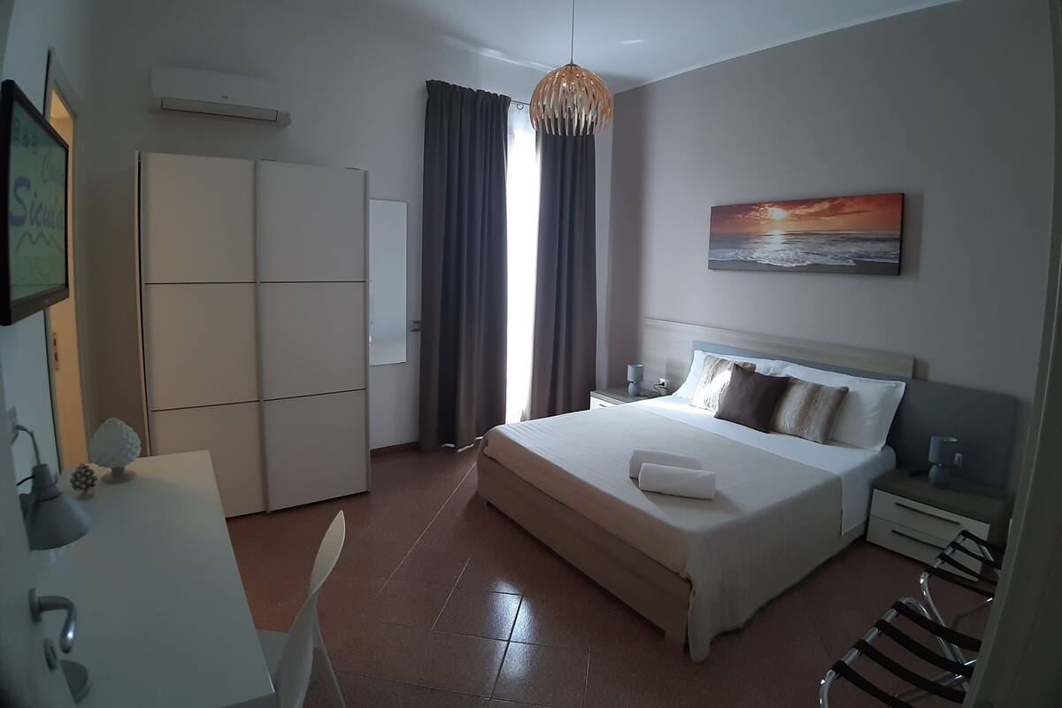 Une chambre d’hôtel avec un lit, une table de chevet, une lampe, une armoire et un tableau représentant un coucher de soleil.