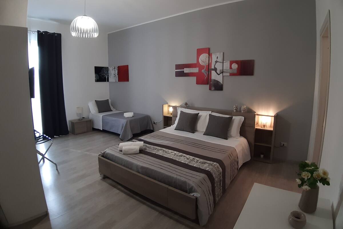 Une chambre moderne avec un grand lit, deux tables de chevet, un luminaire suspendu et des œuvres d’art abstraites accrochées au mur.