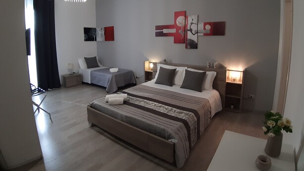 A modern bedroom with a large bed, two bedside tables, a hanging light fixture, and abstract wall art. - Costa Sicula (Avola)