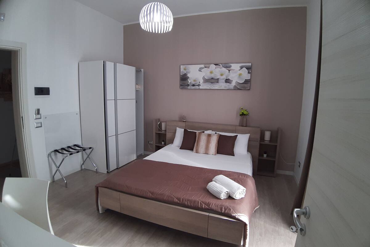 Une chambre à coucher moderne, comprenant un lit, une armoire, une table de chevet et un luminaire suspendu.