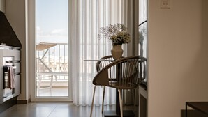 A modern kitchen with a built-in oven and a dining area with a chair and a vase of flowers. - The Sliema Suites (Sliema)