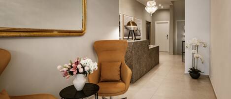 A modern lobby with a reception desk, a seating area with a chair and a small table, and a vase with flowers.