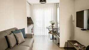 A modern living room with a sofa, a dining table with chairs, a TV mounted on the wall, and a kitchen area in the background. - The Sliema Suites (Sliema)