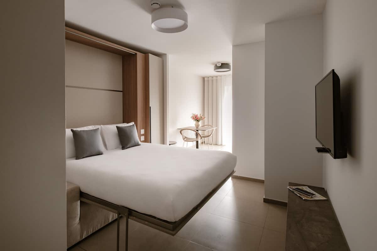 A modern hotel room with a large bed, a flat-screen TV mounted on the wall, and a small table with chairs in the corner.