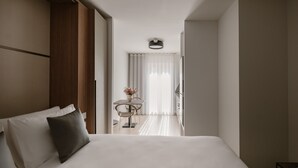 A modern hotel room with a large bed, a small table with chairs, a vase of flowers, and a view of the hallway. - The Sliema Suites (Sliema)