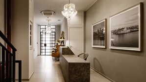 A modern reception area with a marble counter, a chandelier, and framed cityscape photographs on the wall. - The Sliema Suites (Sliema)