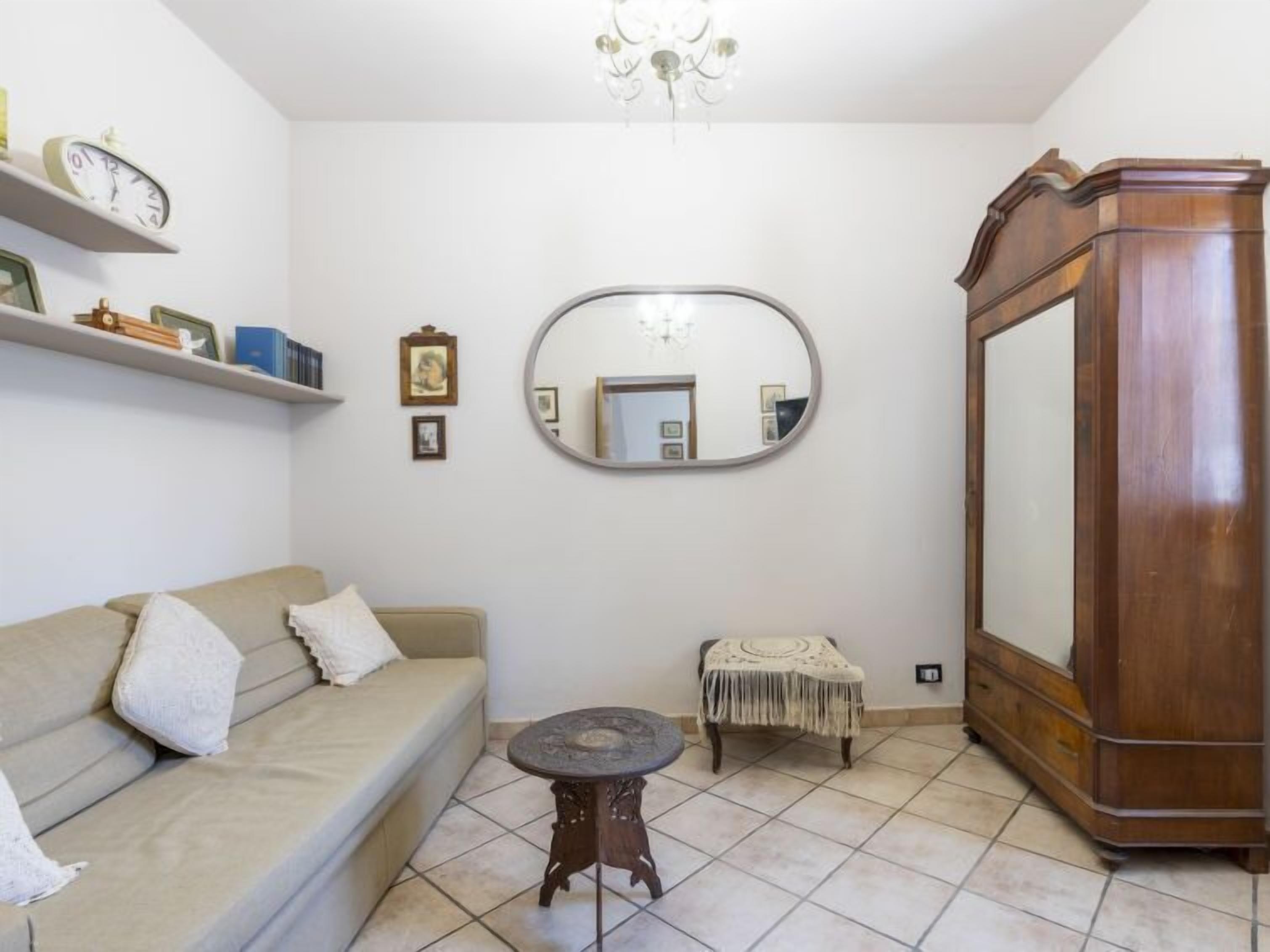Un salon comprenant un canapé, une petite table ronde, un miroir, une commode et un lustre.