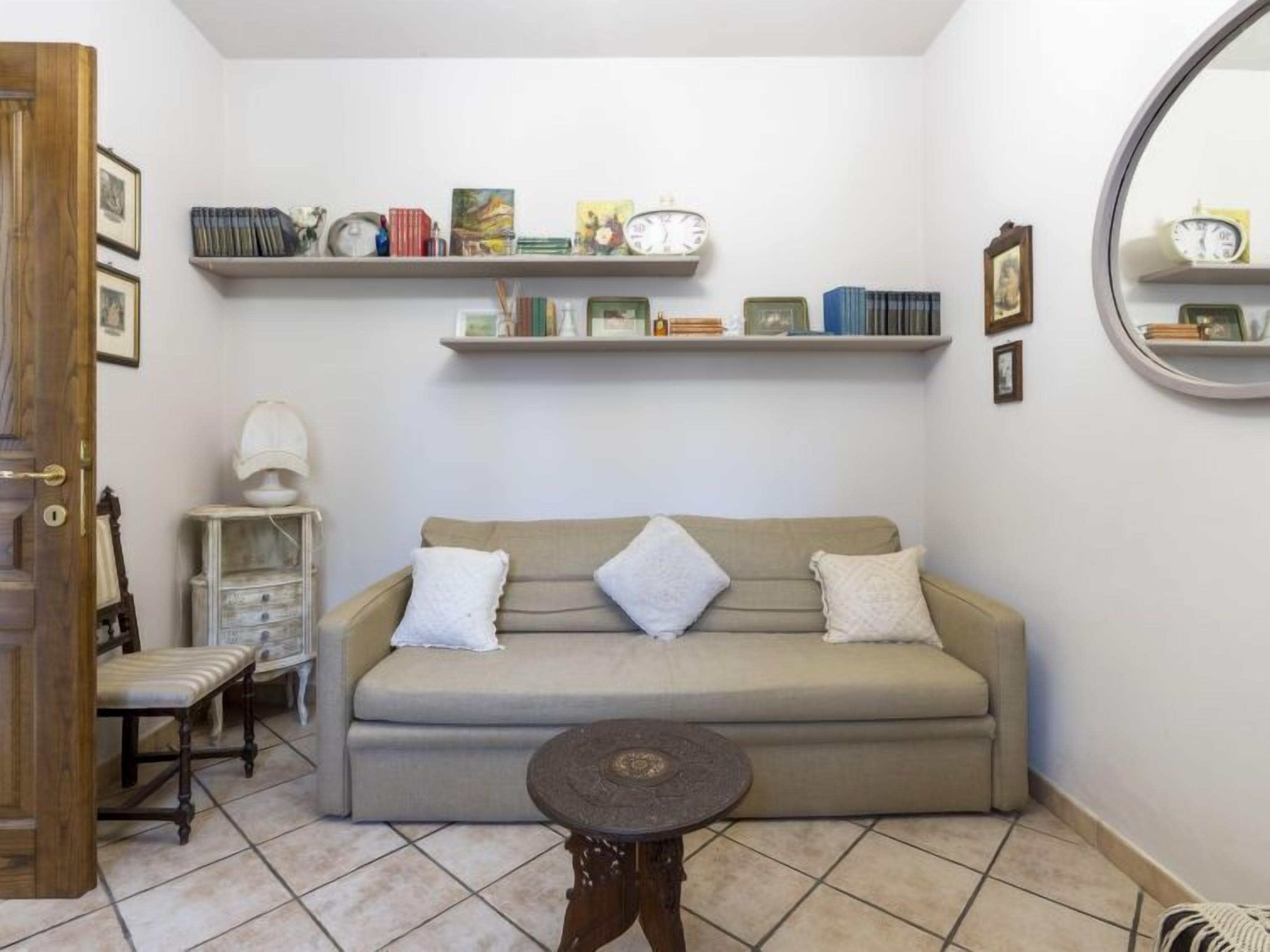 Ein gemütliches Zimmer mit einer Couch, einem kleinen Tisch und Regalen mit Büchern und Dekoration.