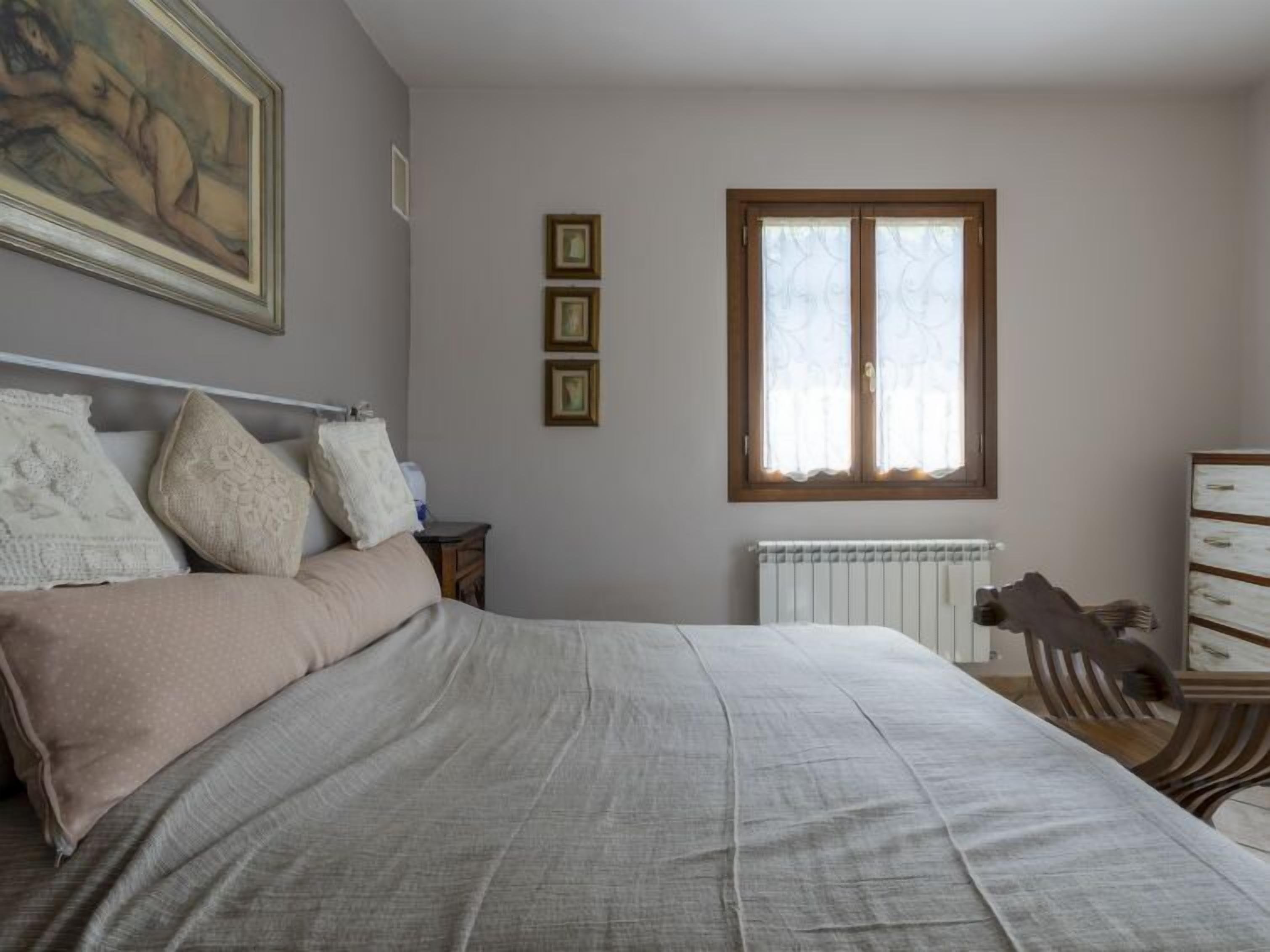 A bedroom with a bed, a dresser, a window, and a radiator.