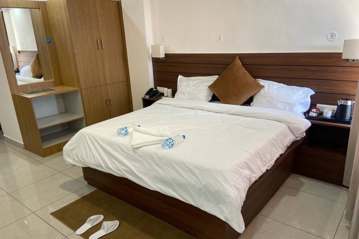 A hotel room with a bed, a wardrobe, a nightstand, and a pair of slippers on the floor.