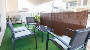 Een terras buiten met een tafel en stoelen, een overdekt gedeelte en een uitzicht op gebouwen op de achtergrond.