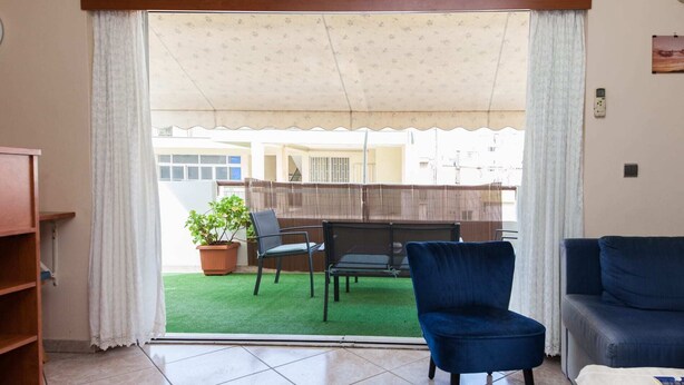 Een woonkamer met een schuifdeur naar een balkon met een groen gazon en een houten omheining.