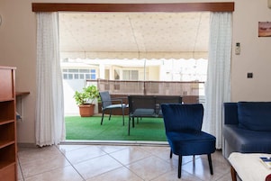Un salón con puerta de vidrio corrediza que da a un balcón con césped verde y valla de madera.