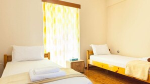Een hotelkamer met twee eenpersoonsbedden, houten hoofdeinden, een klein nachtkastje en een raam met gordijnen.