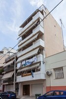 Un edificio de varios pisos con balcones, una bandera visible y una tienda cerrada con persiana.