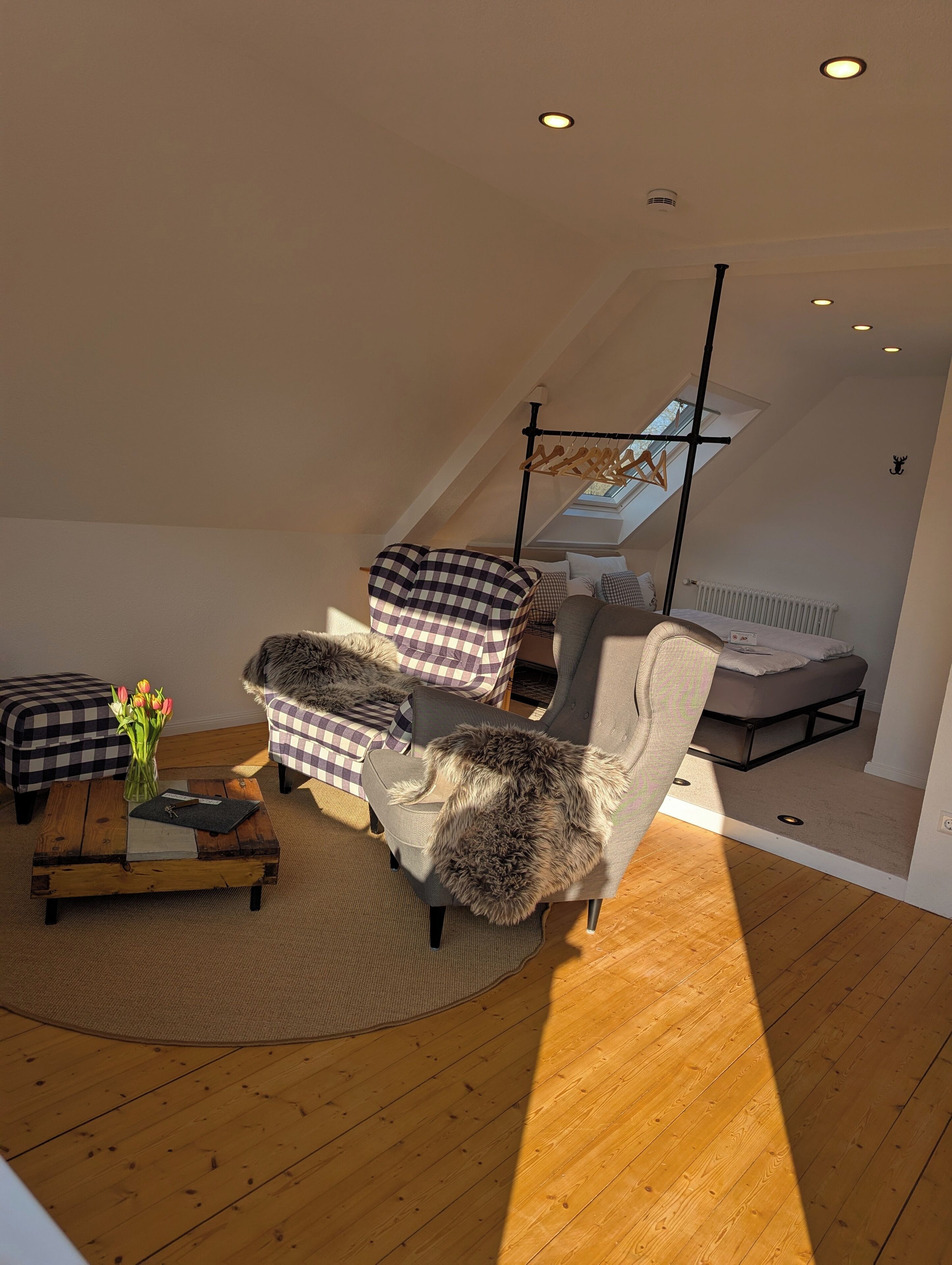 Ein modernes Schlafzimmer im Lofts Stil mit schrägem Dach, Oberlicht, einem Bett und einer Sitzecke mit karierter Möblierung.