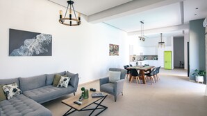 Un salon moderne avec un canapé gris, une table basse et un coin repas agrémenté d’un réfrigérateur vert.