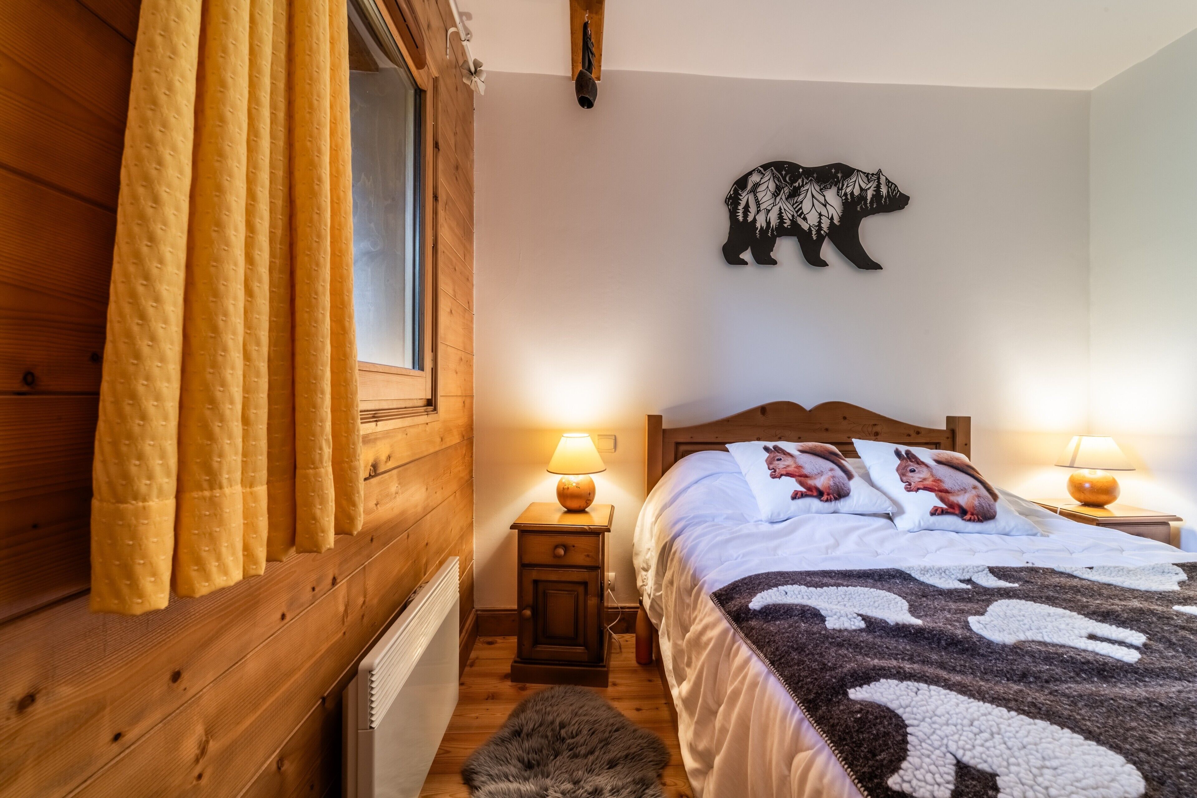 A cozy bedroom with a wooden headboard, a bear wall decoration, two bedside lamps, and a blanket with animal prints.