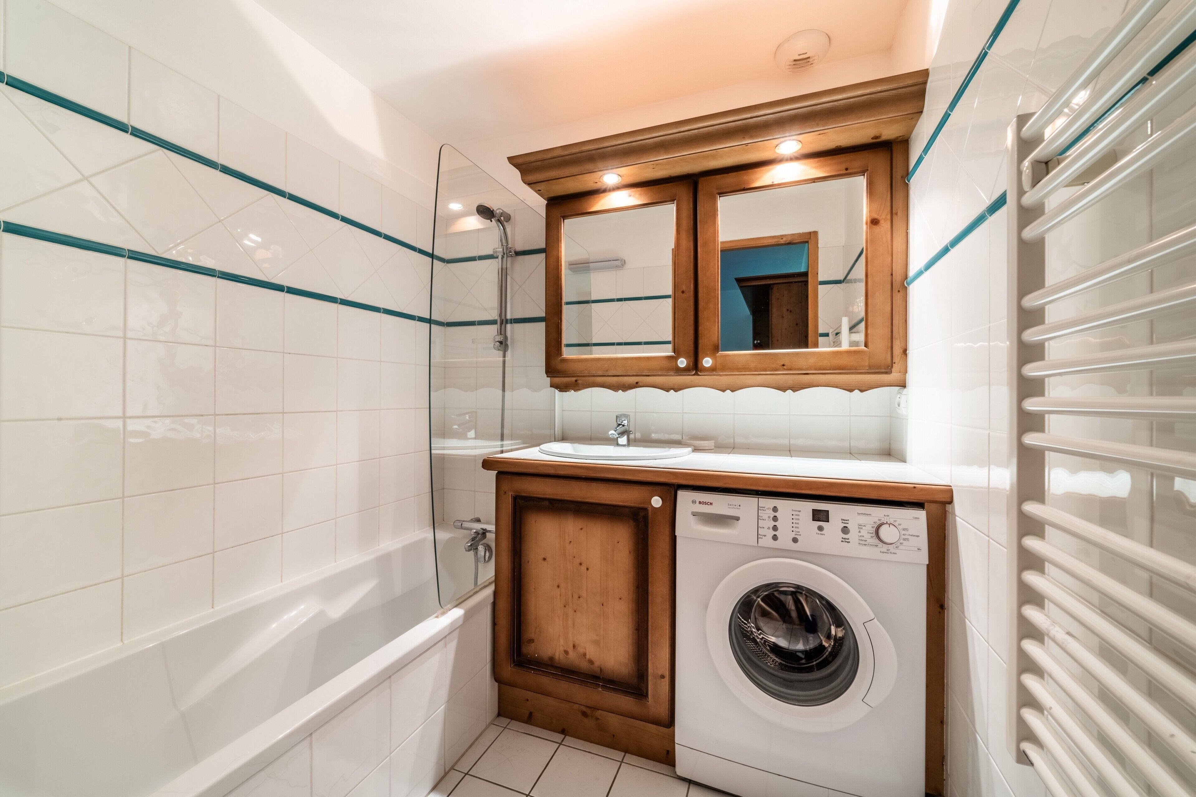 A compact bathroom with a bathtub, a washing machine, a sink, and a mirror above the sink.