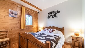 Een houten kamer met een bed, een stoel, een nachtkastje en een beren decoratie aan de muur.