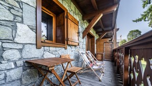 Een stenen gebouw met houten ramen en een houten terras met loungestoelen.