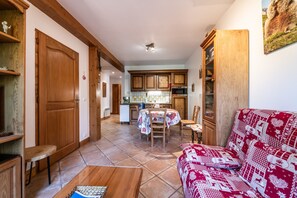 Un salon chaleureux avec un canapé rouge à motifs, des meubles en bois, une table à manger avec des chaises et un coin cuisine doté de meubles en bois et d’un dosseret carrelé.