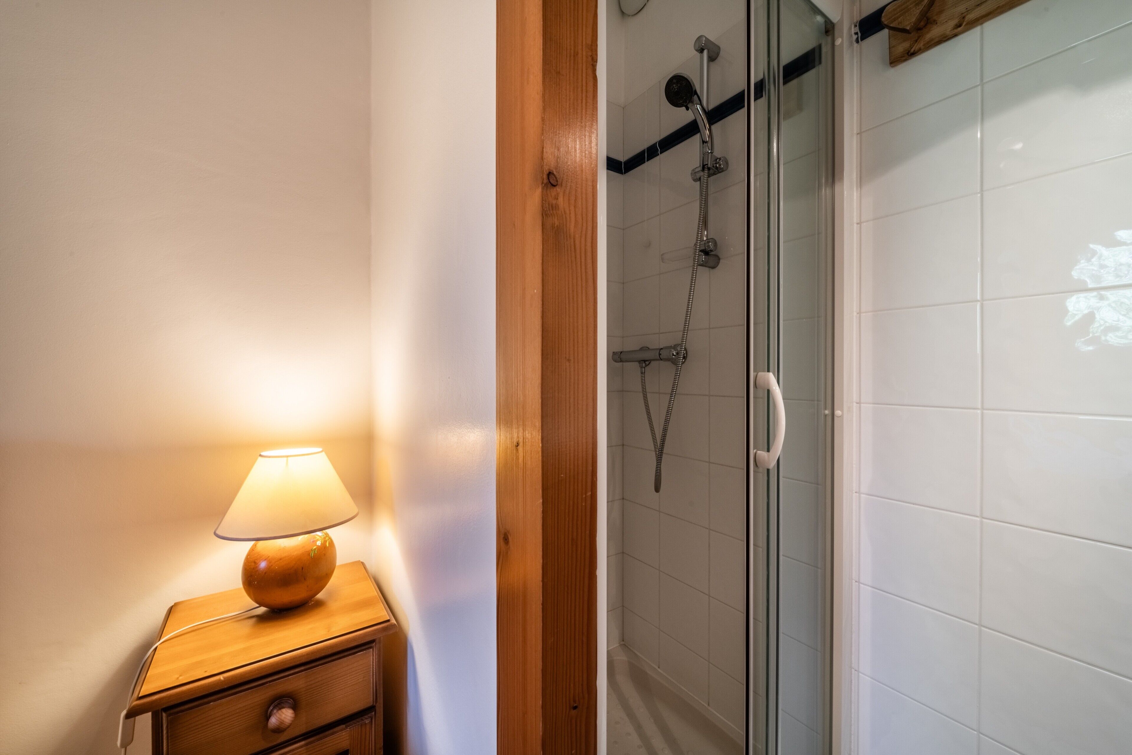 Une salle de bain avec une table de chevet en bois, une lampe et une douche fermée par une paroi de verre.