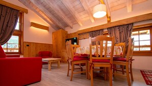 Um quarto aconchegante com paredes de madeira, uma mesa de jantar com cadeiras, um sofá vermelho e uma janela com cortinas.