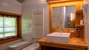 Casa de banho com sanita, bidé, lavatório, espelho, porta-toalhas e janela com vista.
