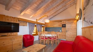 Interior de madeira com uma mesa de jantar, sofá vermelho e uma televisão.