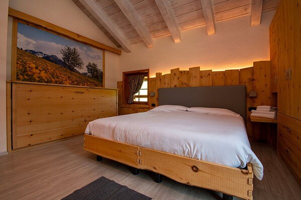 A bedroom with a wooden bed frame, a painting of a landscape, and wooden paneling on the walls.