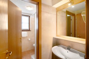 Een badkamer met een houten deur, een wastafel, een spiegel en een raam.