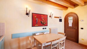 A dining area with a wooden table and chairs, a bench, a wall-mounted painting, and a door with a paper on it. - Apartment 'Chalet Li Palù Trilocale 4' with Mountain View, Balcony and Wi-Fi (Livigno)