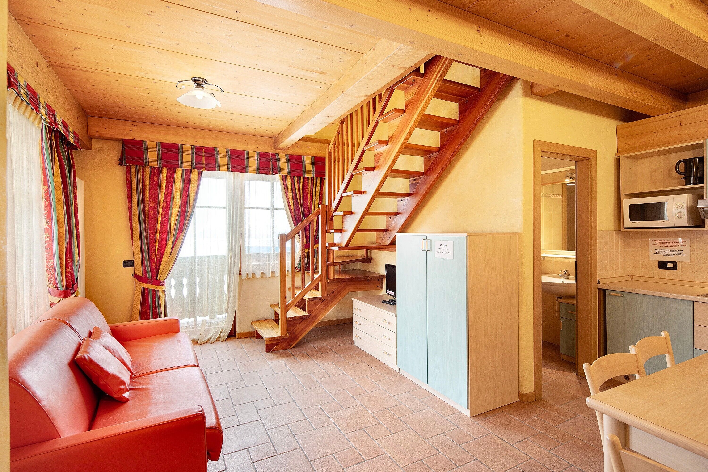 A cozy room with a wooden staircase, a sofa, a dining table, and a kitchen area.