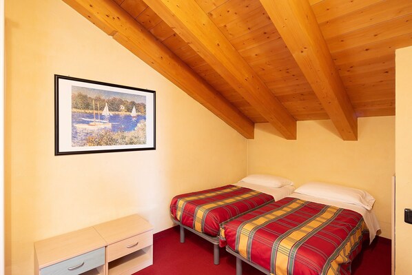 Een slaapkamer met twee bedden, een houten plafond, een lijst met een afbeelding aan de muur en een klein nachtkastje.