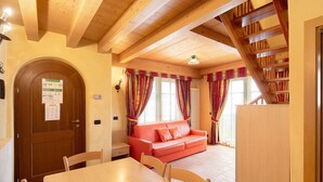 A wooden dining table with chairs, a red sofa, a wooden staircase, and a door with a notice. - Apartment 'Chalet Li Palù Trilocale 4' with Mountain View, Balcony and Wi-Fi (Livigno)
