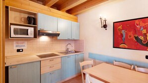 A kitchen with a microwave, stove, sink, and a dining table with chairs. - Apartment 'Chalet Li Palù Trilocale 4' with Mountain View, Balcony and Wi-Fi (Livigno)