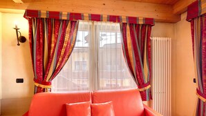 A room with a red sofa, striped curtains, a radiator, and a wall-mounted light fixture. - Apartment 'Chalet Li Palù Trilocale 4' with Mountain View, Balcony and Wi-Fi (Livigno)