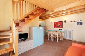 A wooden staircase, a television, a dining table with chairs, a radiator, and a wall-mounted light fixture. - Apartment 'Chalet Li Palù Trilocale 4' with Mountain View, Balcony and Wi-Fi (Livigno)