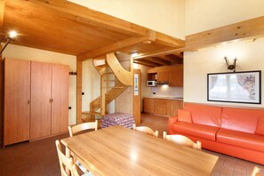 A wooden dining table with chairs, a red sofa, a kitchen area with a microwave, and a staircase.