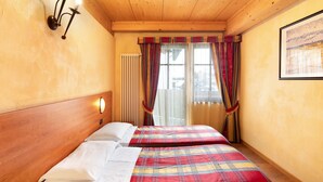 Een kamer met twee bedden, een houten plafond, een wandlamp, een radiator en een raam met gordijnen.