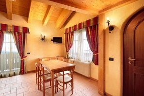A dining area with a wooden table and chairs, a television mounted on the wall, and a door with a handle.