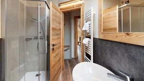 Un baño moderno con ducha de vidrio, lavamanos blanco y detalles de madera.