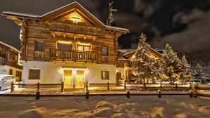 Una cabaña de madera de varios pisos con balcones, un paisaje cubierto de nieve y un cielo nocturno despejado.