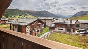 A mountain village with traditional wooden buildings, a clear view of the surrounding hills, and a wooden balcony railing. - Apartment 'Chalet Leur Gusja Golp Trilocale' with Mountain View, Shared Garden and Wi-Fi (Livigno)
