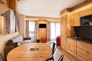 A cozy room with a wooden dining table, chairs, a sofa, a TV, and wooden cabinets.
