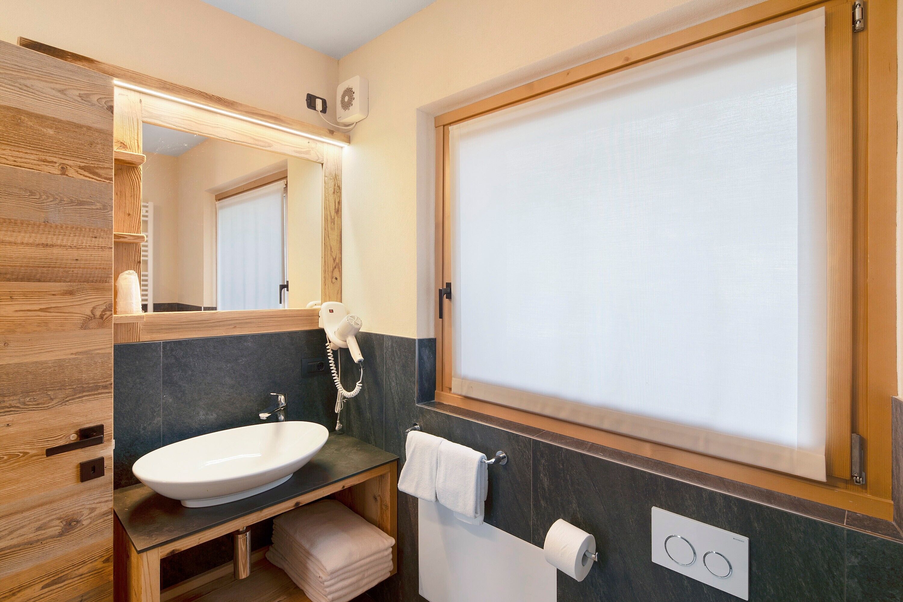 A bathroom with a wooden vanity, a sink, a towel rack, a mirror, and a window with blinds.