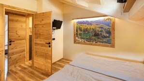 A bedroom with a wooden door, a bed, a mounted TV, and a framed picture of a forest. - Apartment 'Chalet Leur Gusja Golp Trilocale' with Mountain View, Shared Garden and Wi-Fi (Livigno)